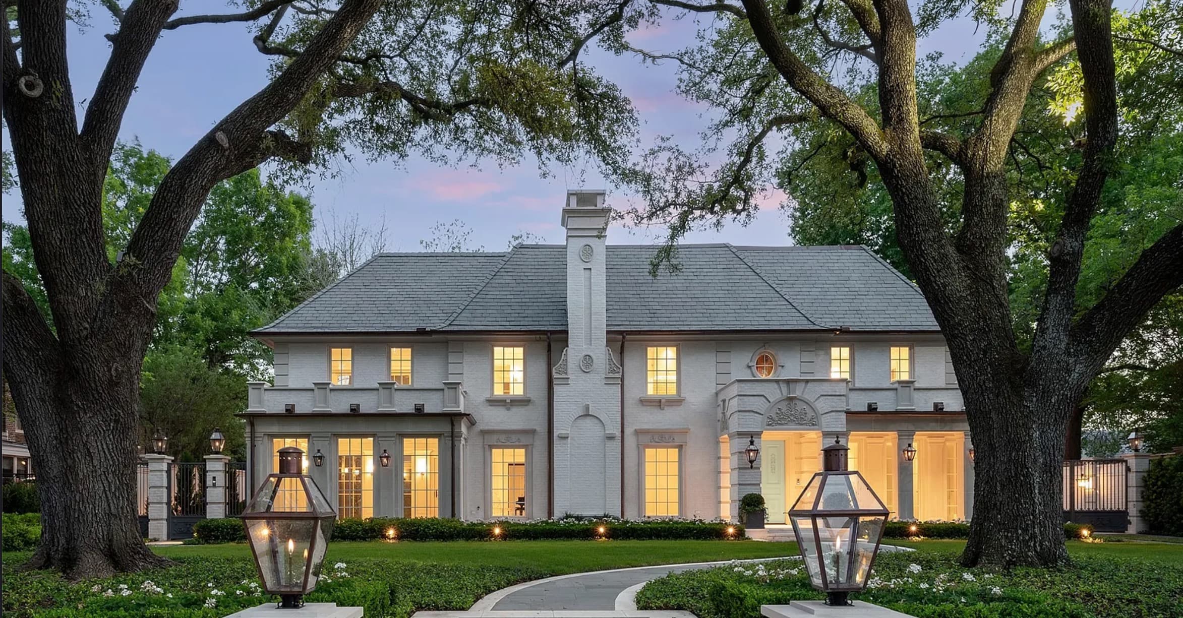 Renovated white brick home at dusk with landscaping and exterior lighting