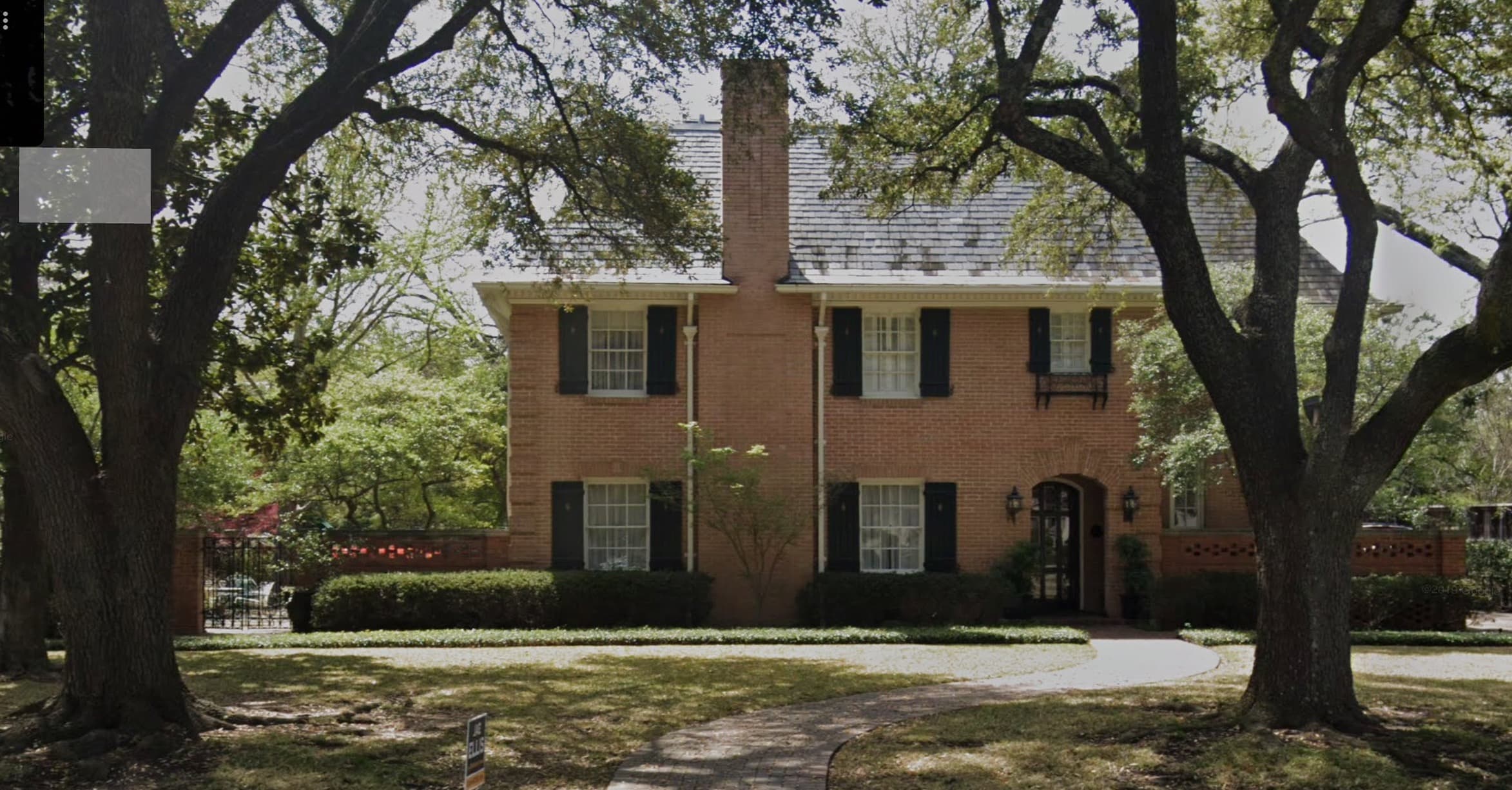 Two-story red brick home before renovation, framed by large oak trees